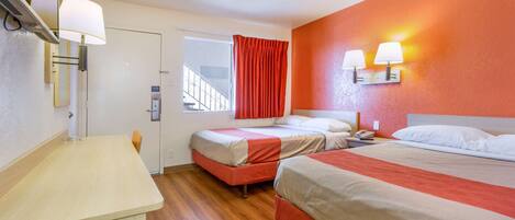A hotel room with two beds, a wooden floor, a desk, a mirror, and two wall-mounted lamps.