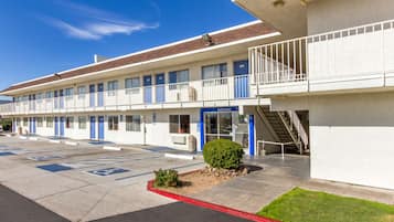 A motel with a parking lot, a small garden, and a staircase leading to the entrance.