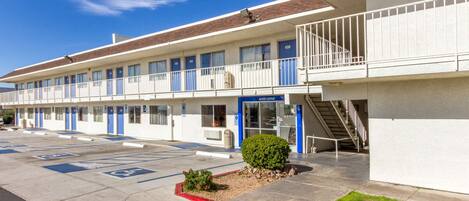 A motel with a parking lot, a small garden, and a staircase leading to the entrance.
