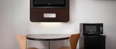 A small room with a round table, two chairs, a wall-mounted TV, and a microwave.