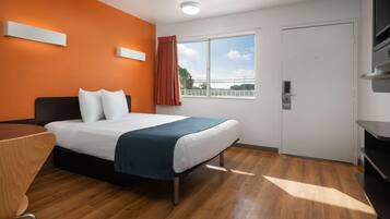 A hotel room with a bed, a desk, a window with curtains, and a door.