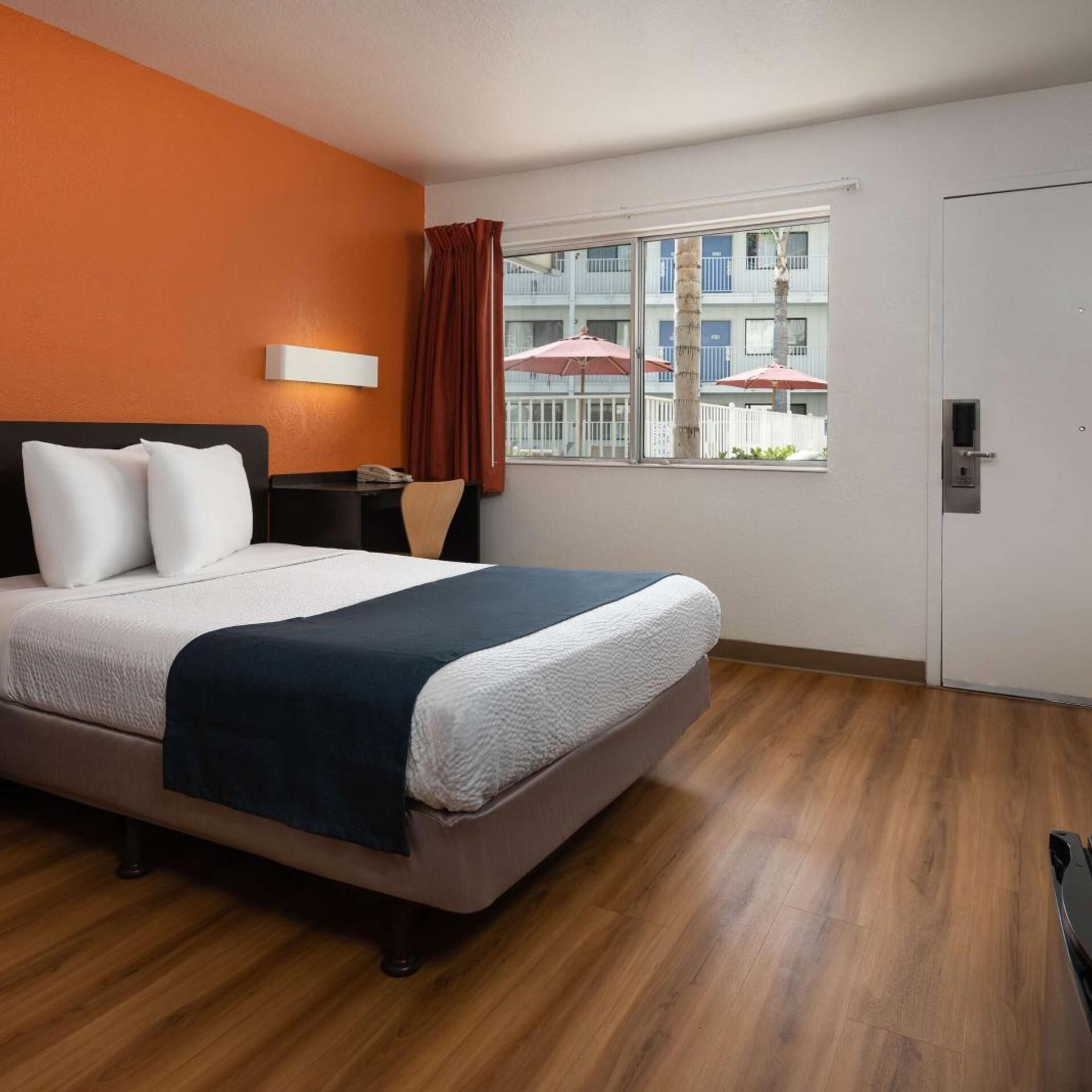 A hotel room with a bed, a nightstand, a window with curtains, and a door.
