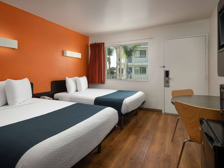 Habitación de hotel con dos camas, un escritorio, una silla y una ventana con cortinas.