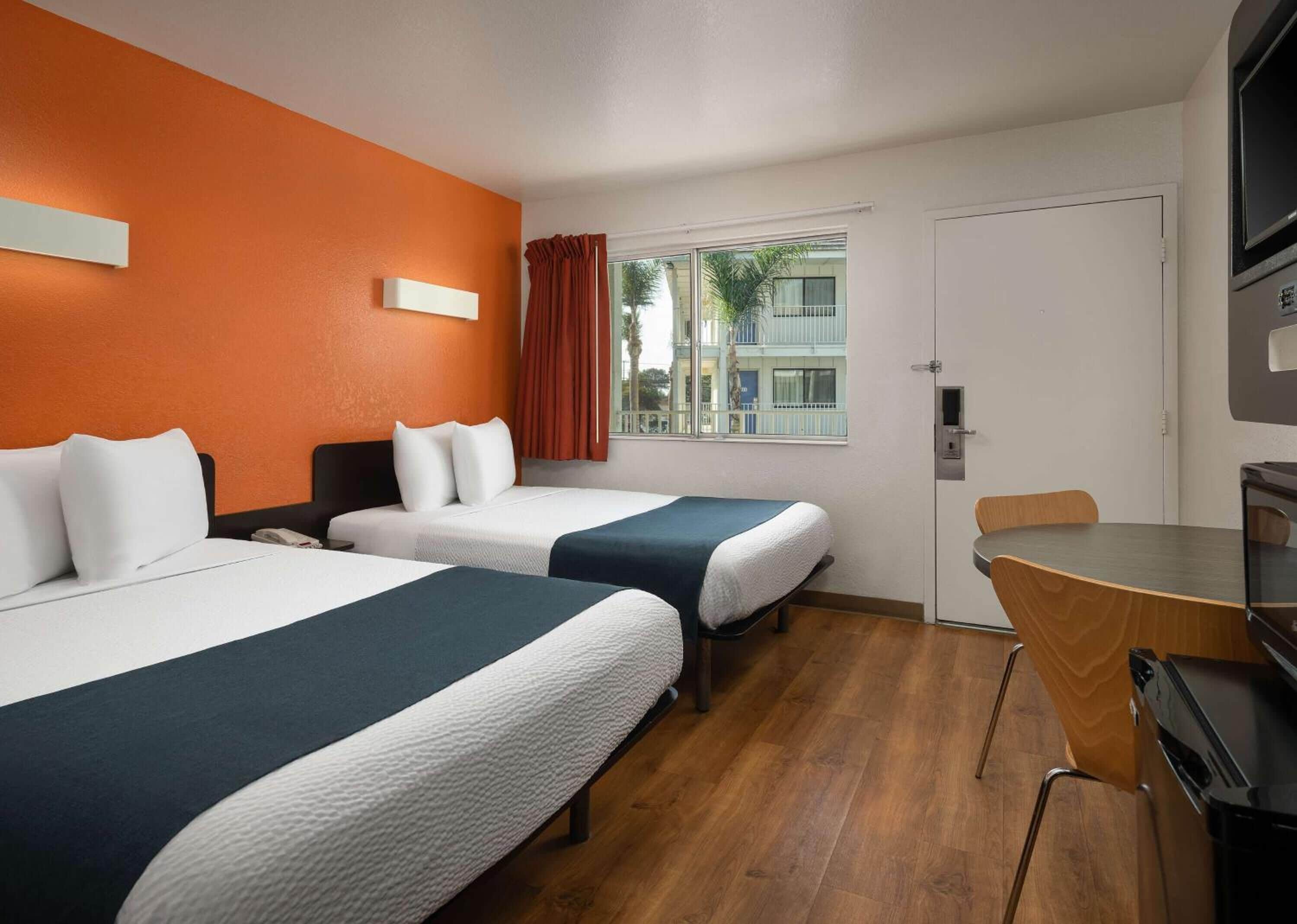 A hotel room with two beds, a desk, a chair, a TV, and a window with curtains.