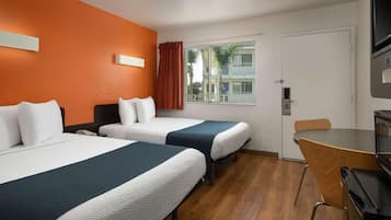 A hotel room with two beds, a desk, a chair, a TV, and a window with curtains.