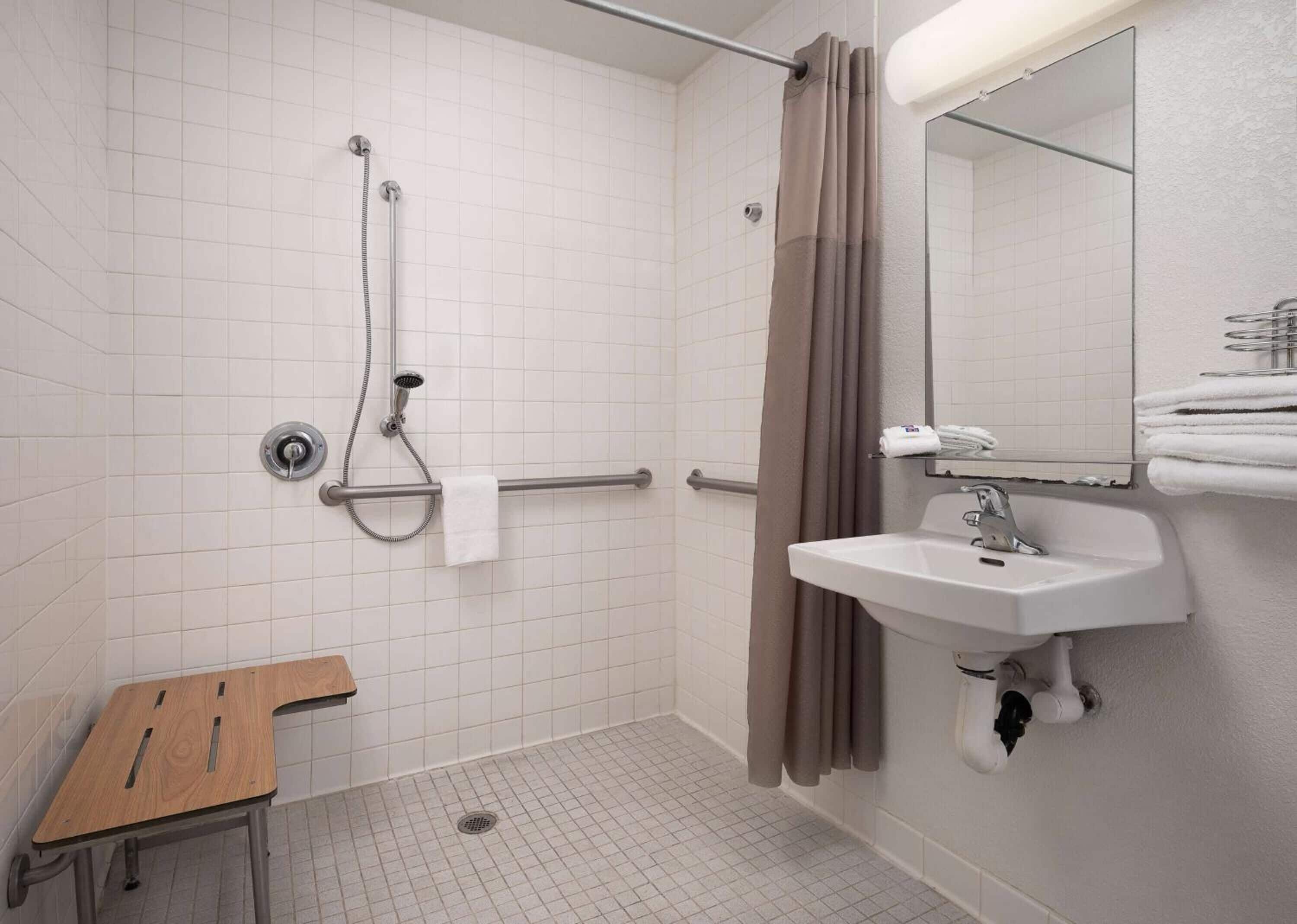 Un baño con ducha, lavabo, espejo y una mesita.