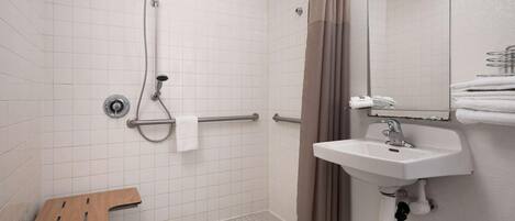 Un baño con ducha, lavabo, espejo y una mesita.