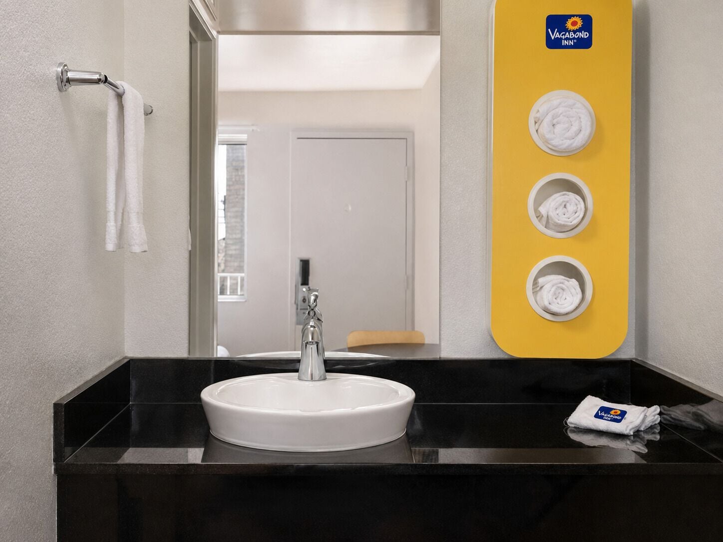 A modern bathroom with a white sink, a mirror, and a yellow towel rack with three towels.