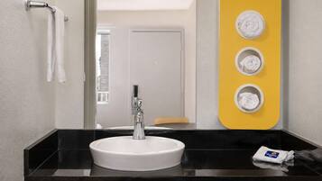 A modern bathroom with a white sink, a mirror, and a yellow towel rack with three towels.
