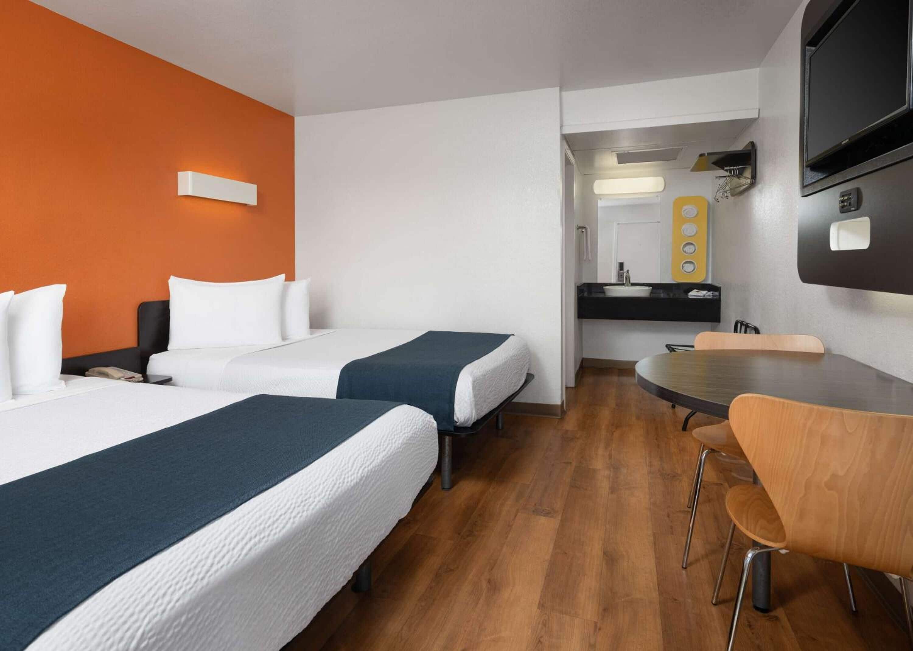 Ein Hotelzimmer mit zwei Betten, einem Esstisch und einem an der Wand befestigten Fernseher.