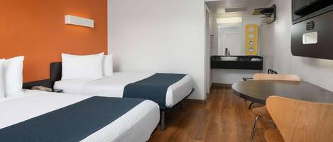 Ein Hotelzimmer mit zwei Betten, einem Esstisch und einem an der Wand befestigten Fernseher.