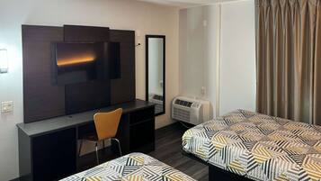 Una habitación de hotel con escritorio, silla, dos camas, televisión y aire acondicionado.