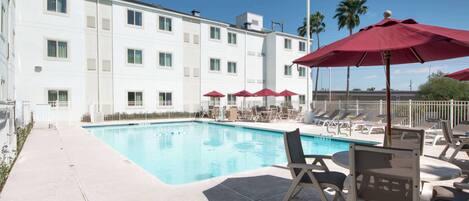 A swimming pool with lounge chairs and umbrellas, surrounded by a white building with multiple windows.