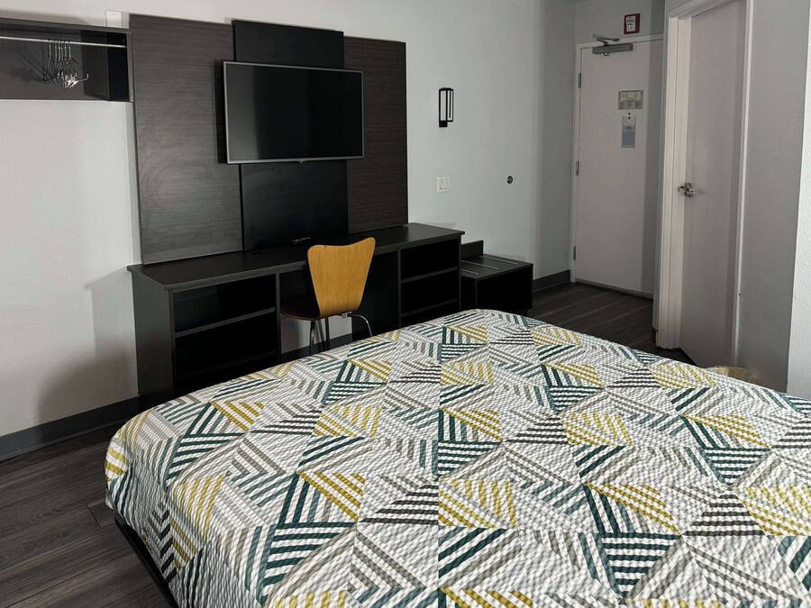 Habitación de hotel con cama, escritorio, silla, televisor y puerta.