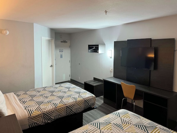 A hotel room with two beds, a desk, a chair, a TV, and a door.