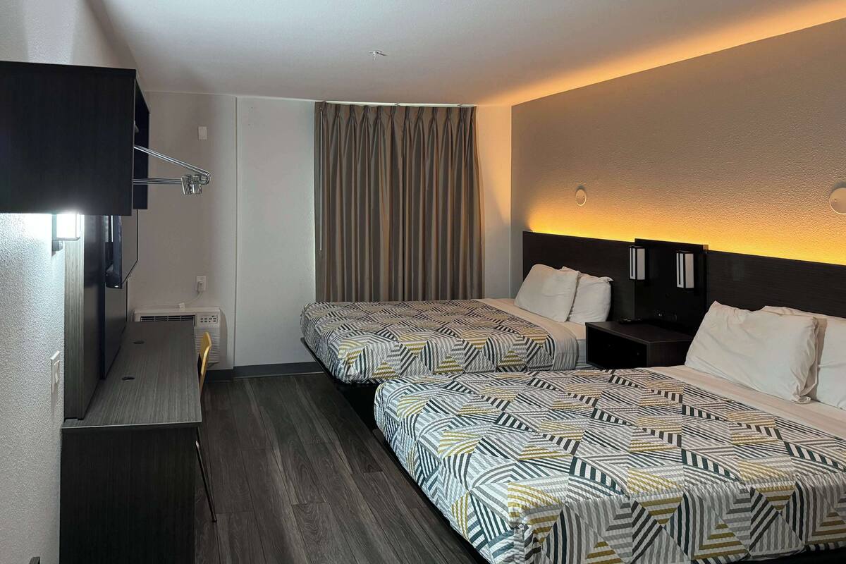 Une chambre d’hôtel avec deux lits, un bureau, une télévision et un rideau.