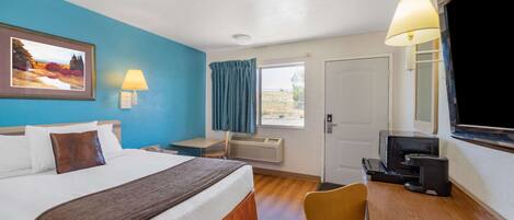 A hotel room with a bed, desk, chair, TV, and a window with curtains.