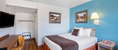 Une chambre d’hôtel avec un lit, un bureau, une chaise, une télévision et deux tableaux encadrés au mur.