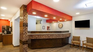 A reception area with a tiled counter, wooden chairs, a clock, and a flat-screen TV mounted on the wall. - Travelodge by Wyndham Miles City (Miles City)