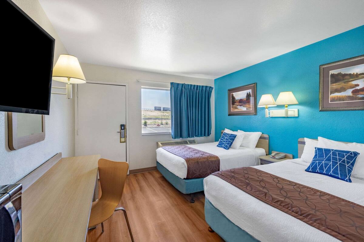 A hotel room with two beds, a desk, a TV, and a window with curtains.