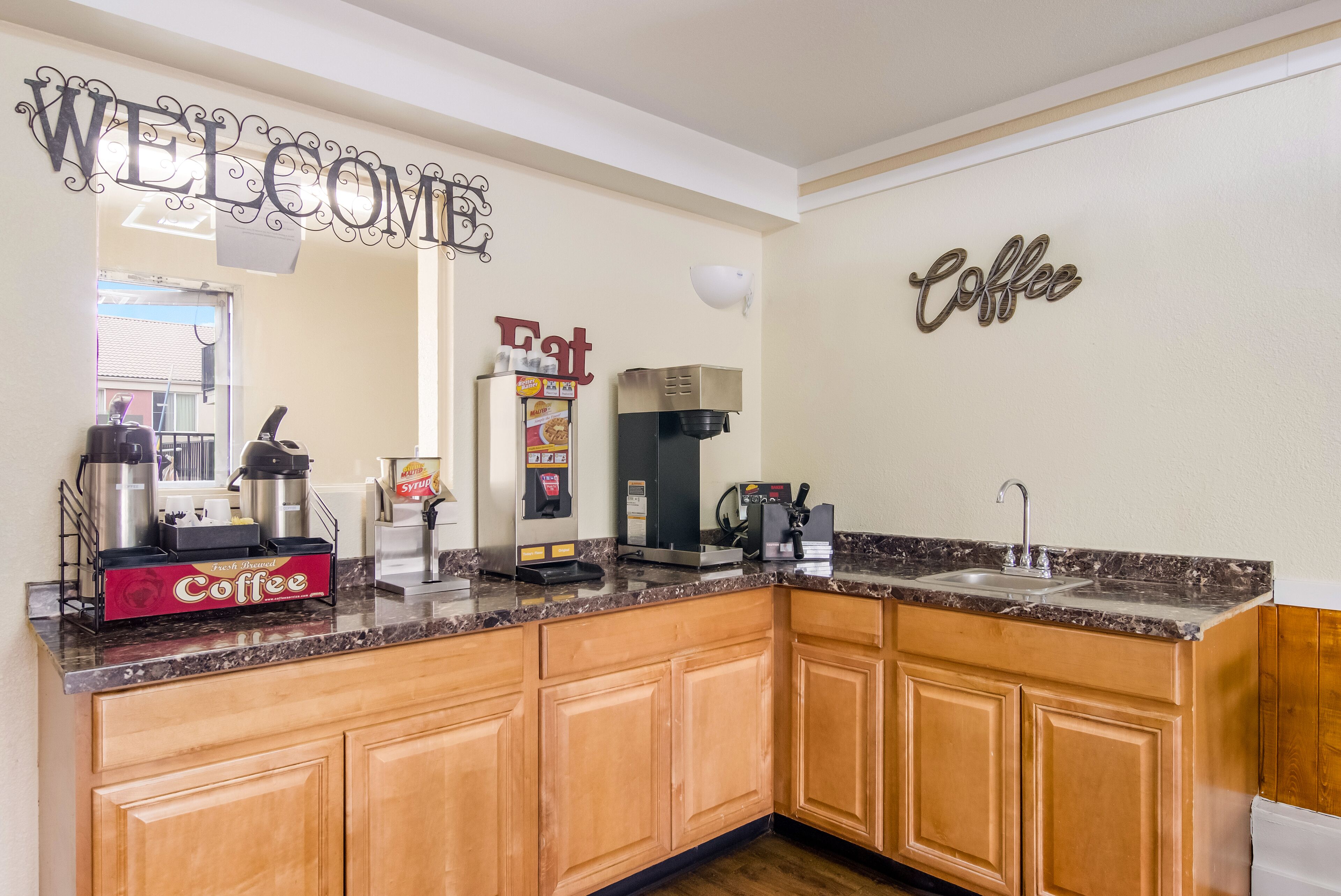 A kitchen with a coffee station, a welcome sign, and a coffee sign on the wall.