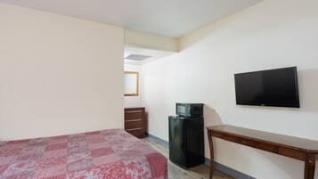 A bedroom with a bed, a desk, a television, and a refrigerator.