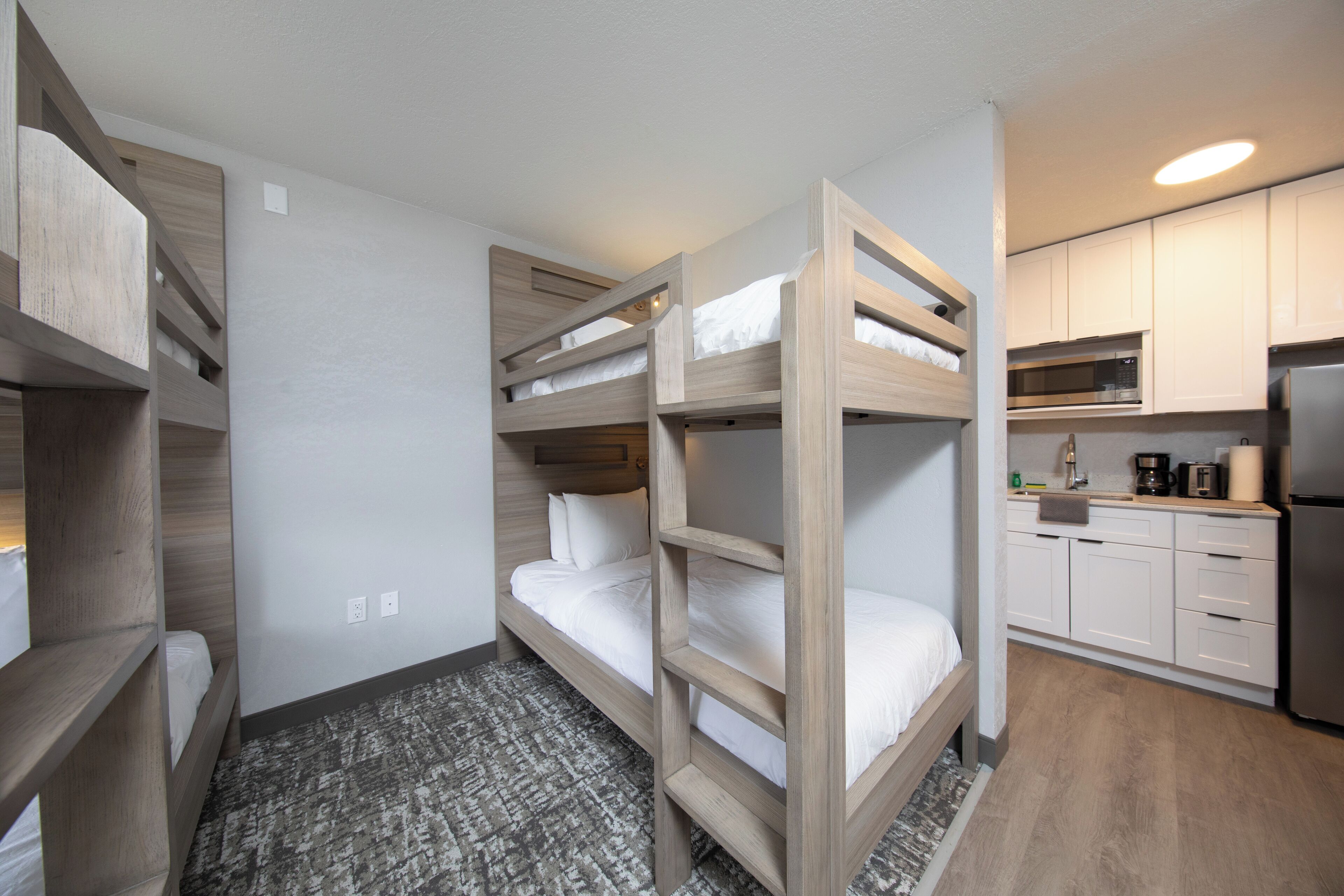 Ein kleines Hotelzimmer mit Etagenbetten, einer Küchenzeile und einem gemusterten Teppich.