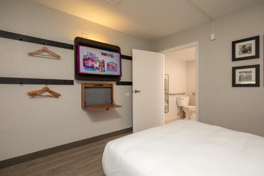 Een hotelkamer met een bed, een aan de muur bevestigde televisie, een houten plank en een deur naar een badkamer.