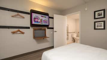 Een hotelkamer met een bed, een aan de muur bevestigde televisie, een houten plank en een deur naar een badkamer.