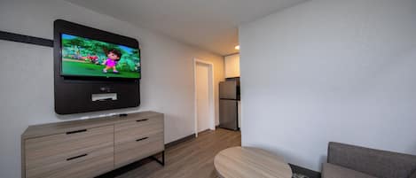 A modern living room with a flat-screen TV mounted on the wall, a wooden cabinet, a round wooden table, and a grey sofa.