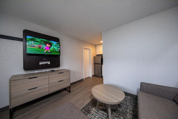 A modern living room with a flat-screen TV mounted on the wall, a wooden cabinet, a round wooden table, and a grey sofa. - The Jackson SouthTown (Jackson)