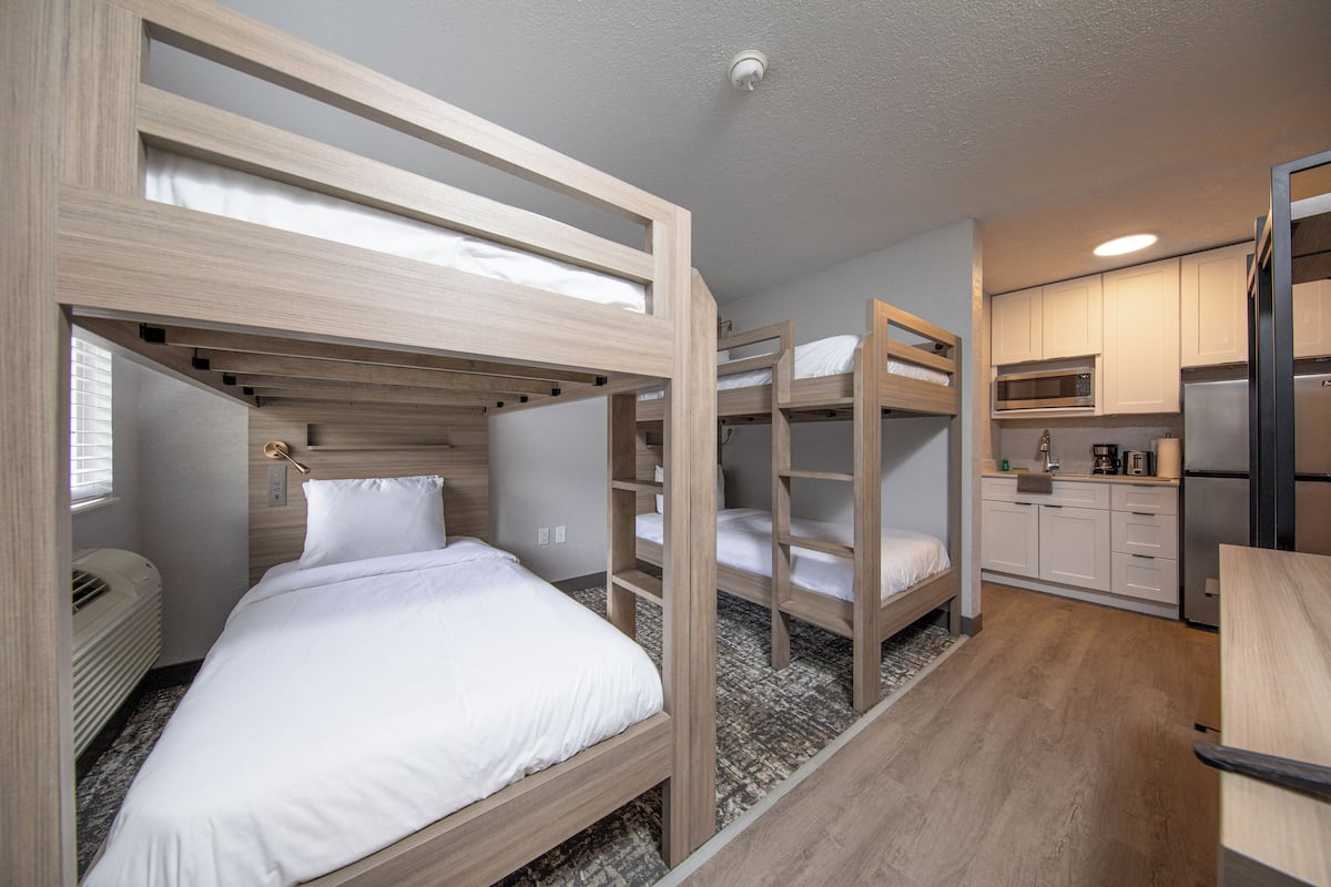 A bunk bed room with a kitchen area, including a microwave and refrigerator.