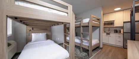 A bunk bed room with a kitchen area, including a microwave and refrigerator.