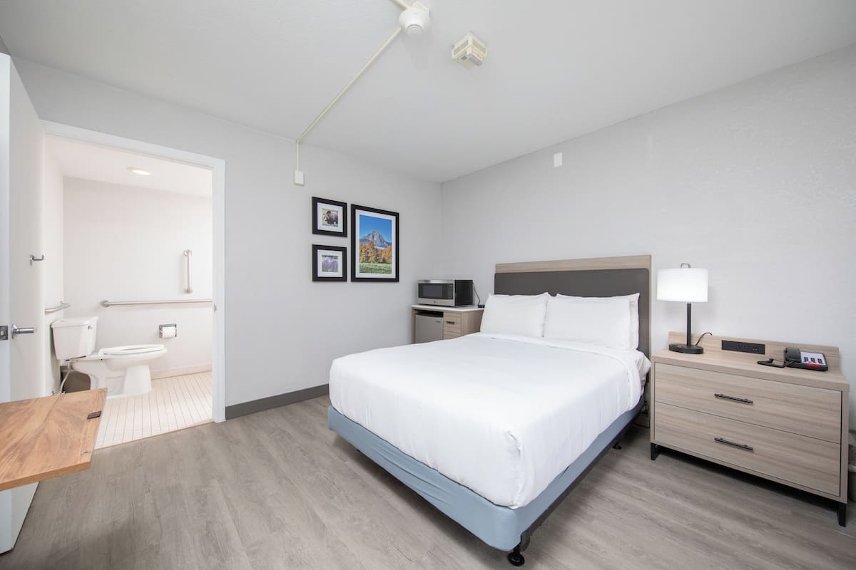 A hotel room with a bed, bedside table, lamp, and a small desk with a chair.