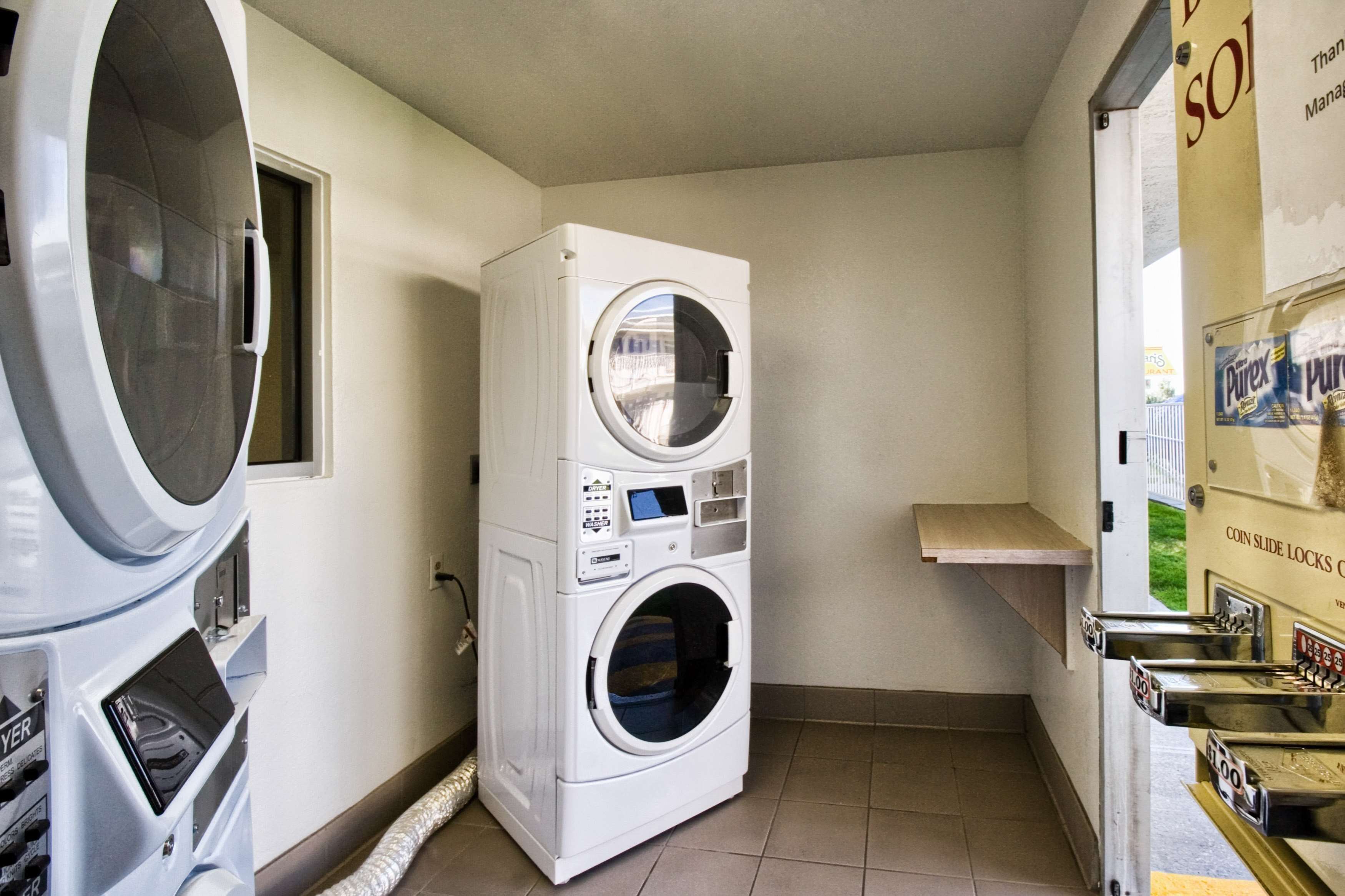 Een wasserette met gestapelde wasmachines en drogers, een droger op afstand en een bord aan de muur.