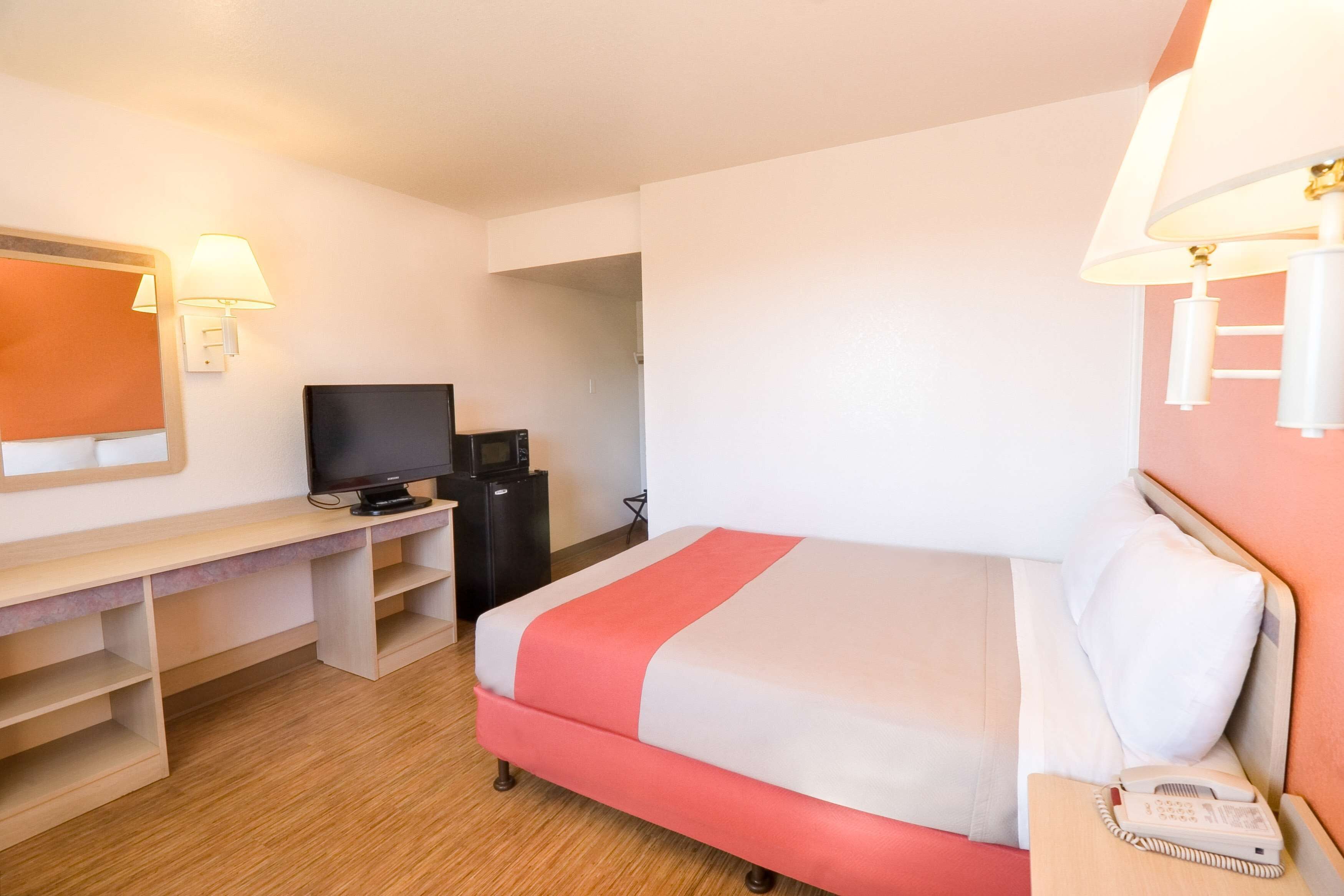 A hotel room with a bed, a desk with a television, a telephone, and a lamp.