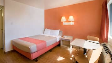 A hotel room with a bed, bedside table, chair, table, and a wall-mounted lamp.