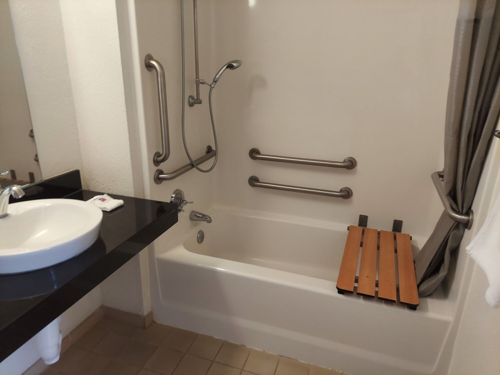 A bathroom with a white sink, a bathtub, and grab bars.