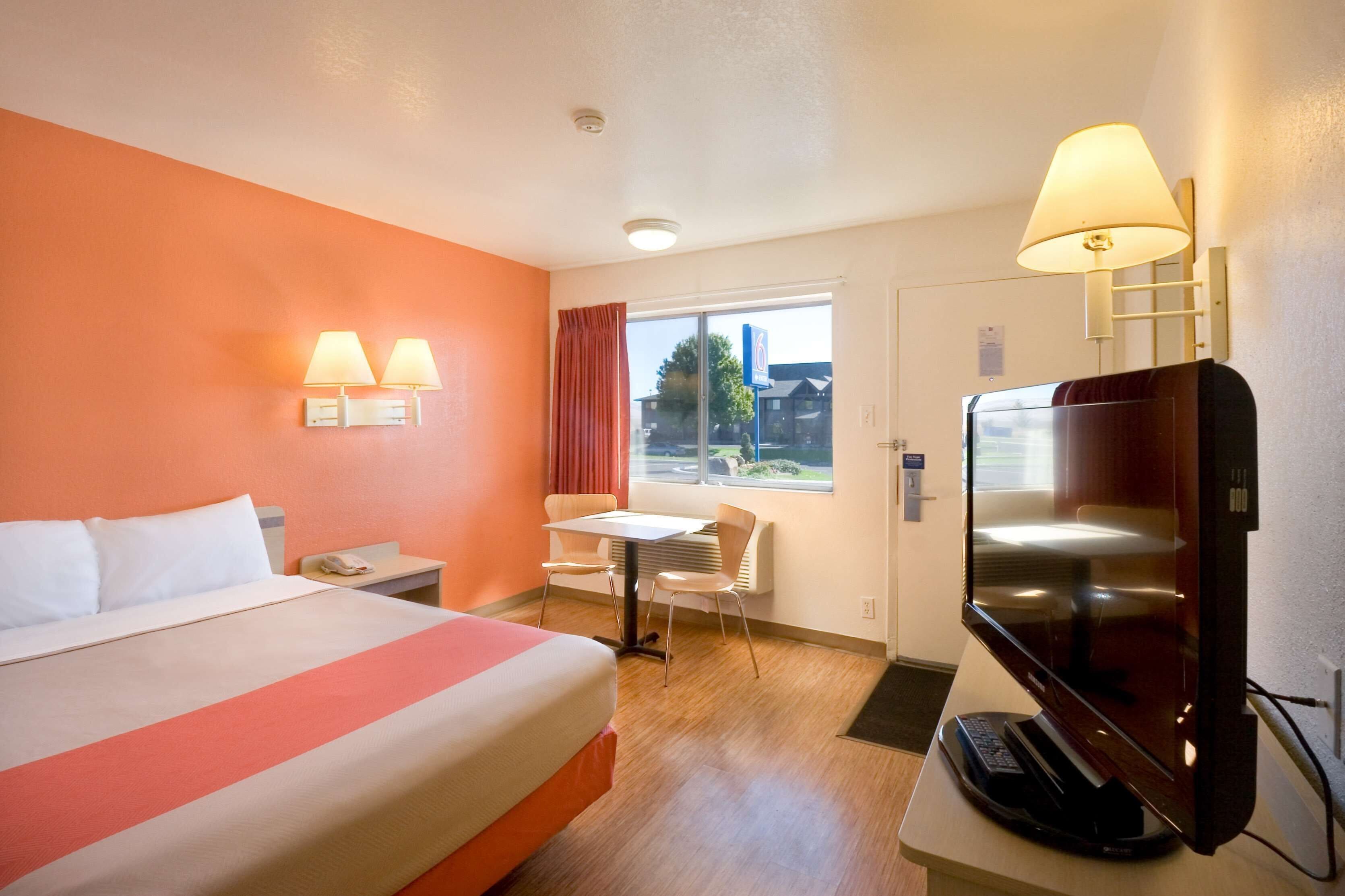 A hotel room with a bed, a desk, a chair, a TV, and a window with curtains.