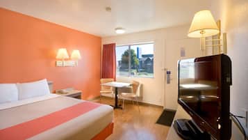 Ein Hotelzimmer mit Bett, Schreibtisch, Stuhl, Fernseher und einem Fenster mit Vorhängen.