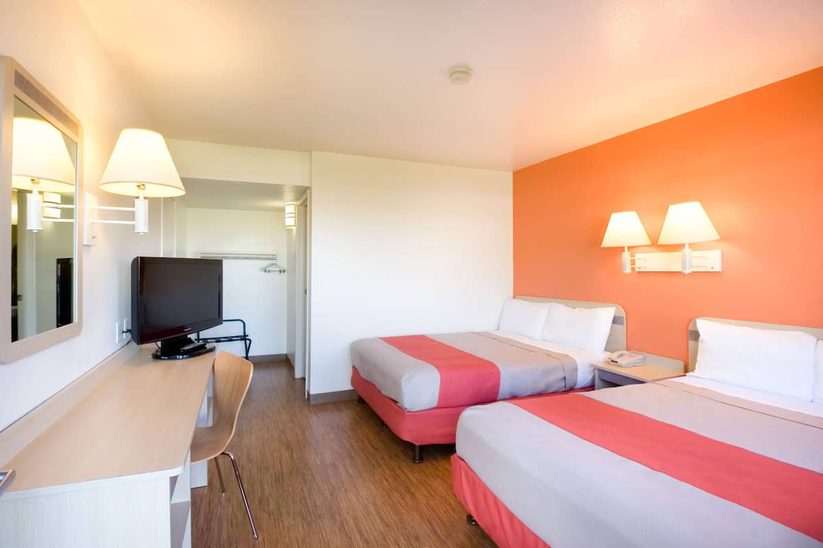 A hotel room with two beds, a desk, a television, and a mirror.