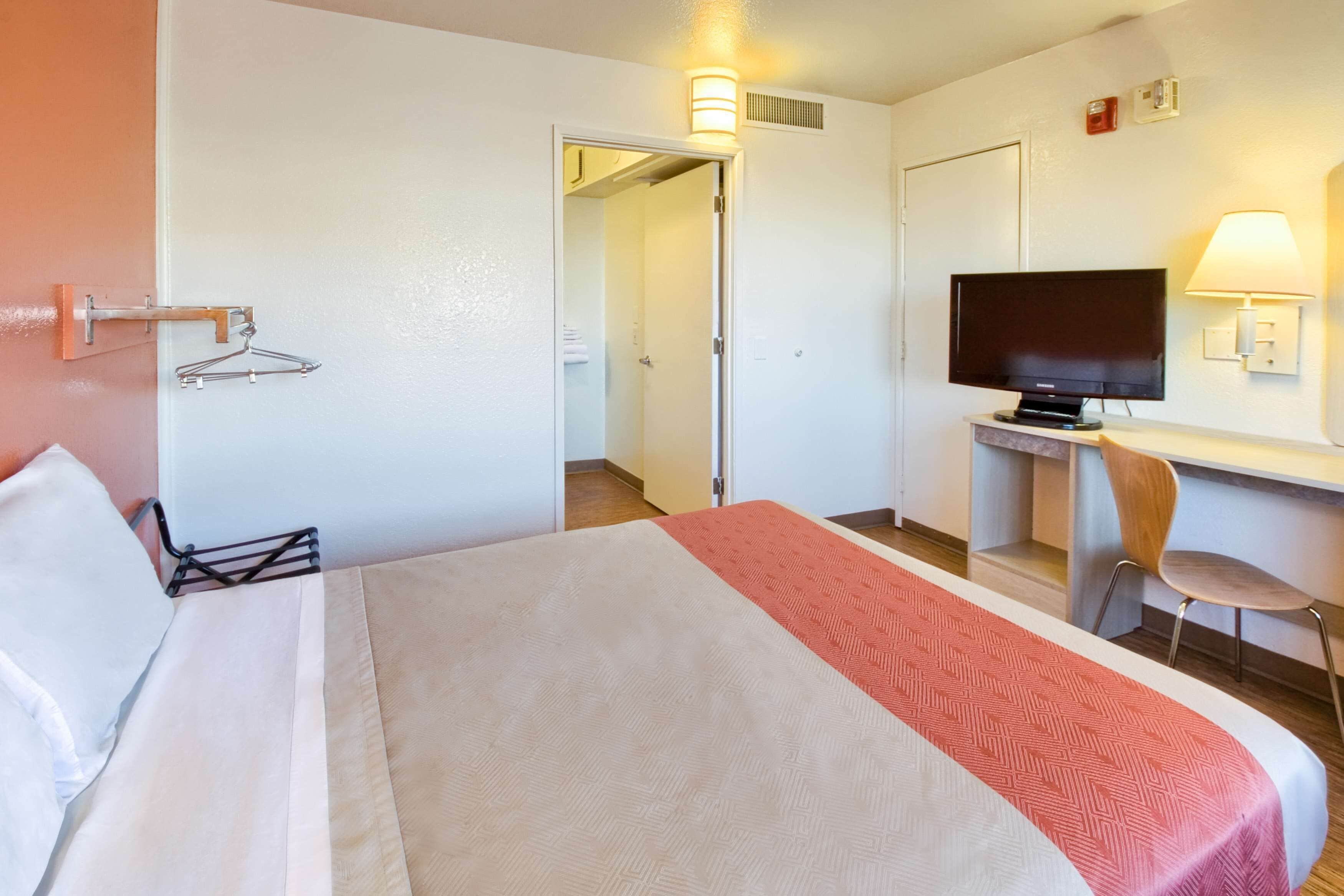 A hotel room with a bed, a desk with a television, a chair, and a door leading to a bathroom.