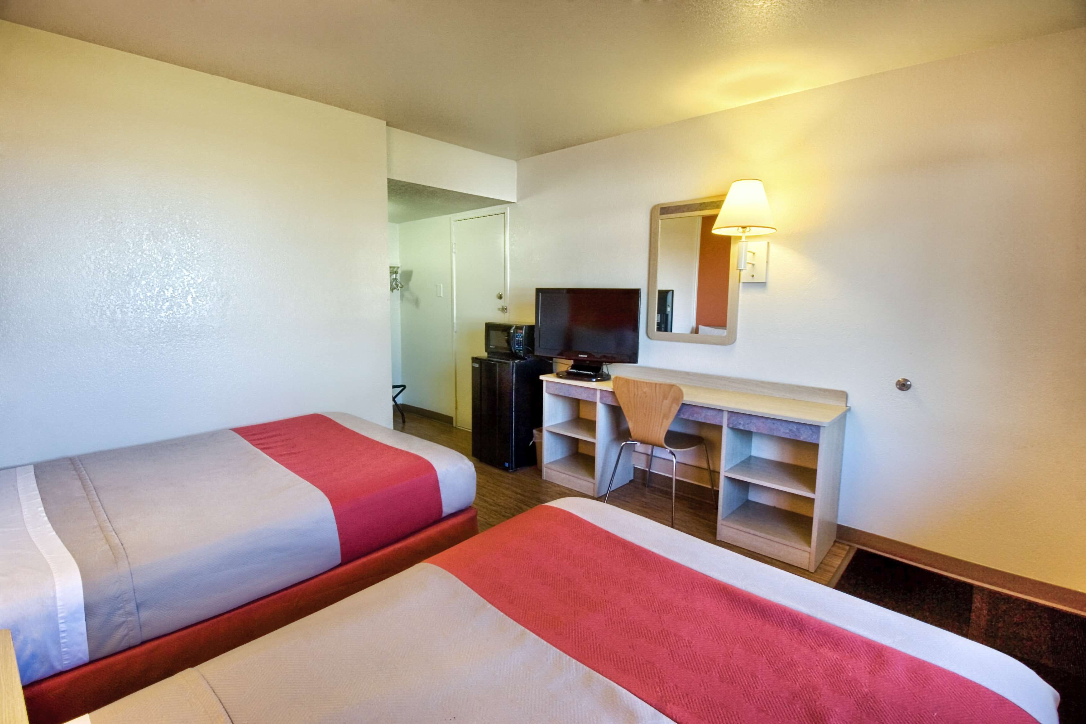 A hotel room with two beds, a desk, a chair, a TV, and a mirror.