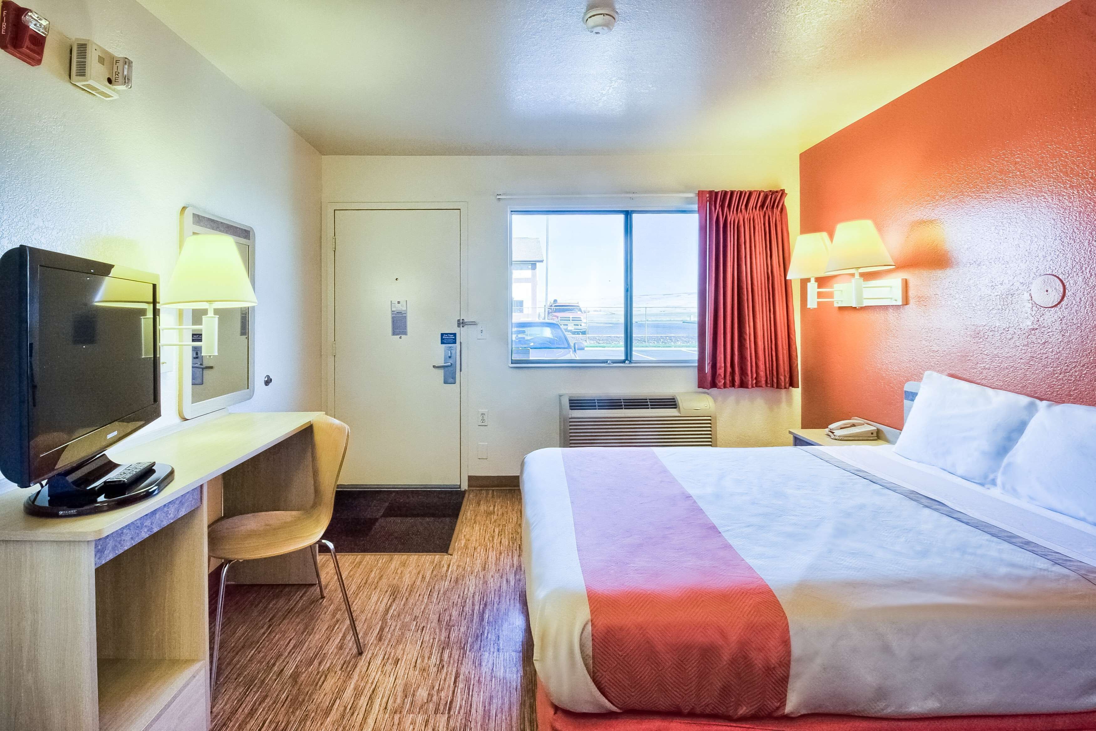 A hotel room with a bed, desk, chair, TV, and window.