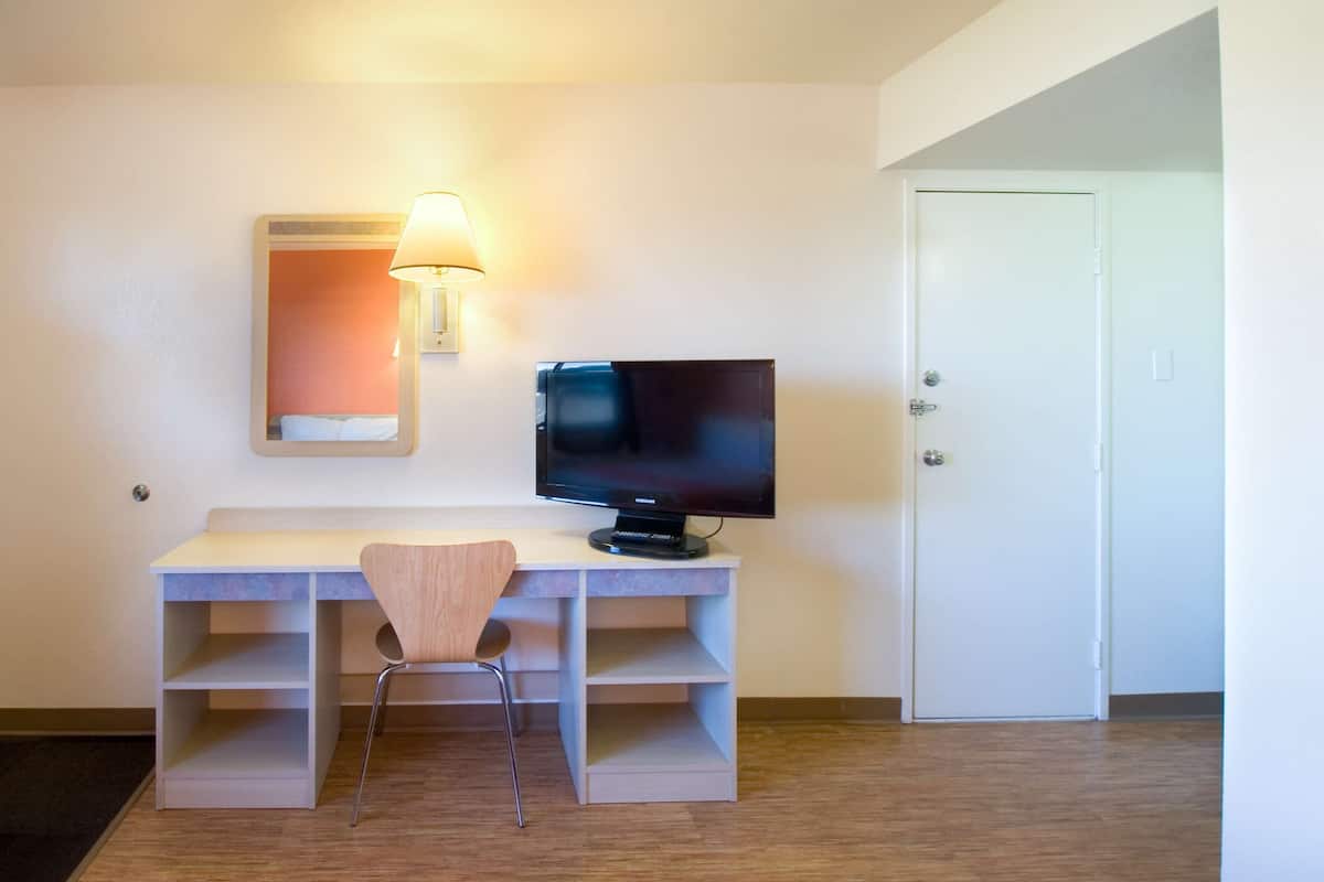 A hotel room with a desk, chair, television, and a door.