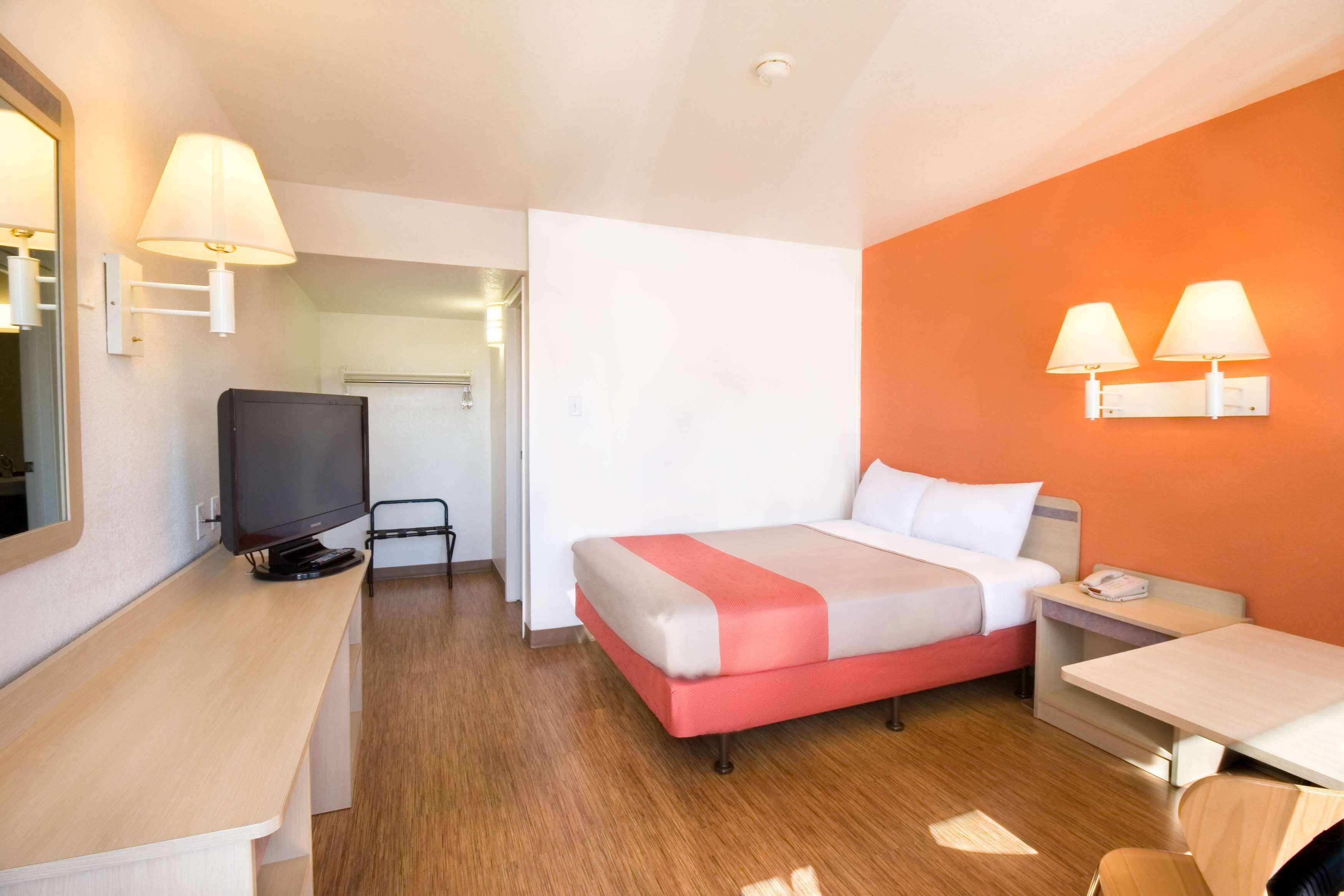 A hotel room with a bed, a desk, a TV, and two wall-mounted lamps.