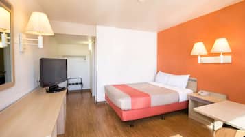 A hotel room with a bed, a desk, a TV, and two wall-mounted lamps.