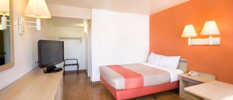 A hotel room with a bed, a desk, a TV, and two wall-mounted lamps.