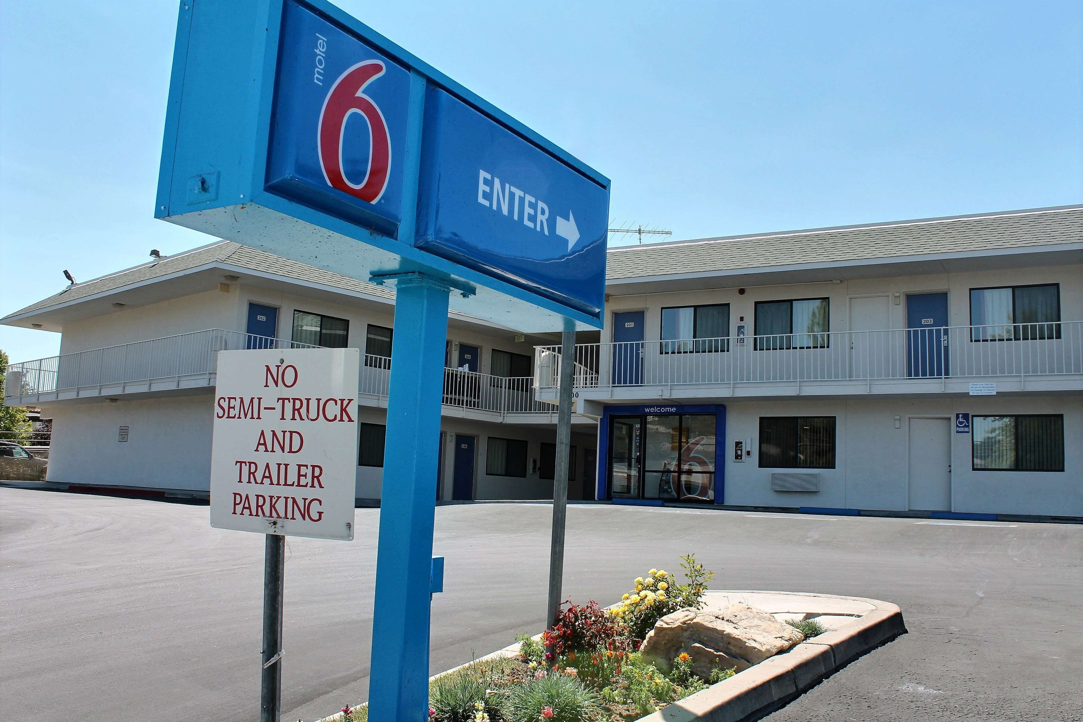 A motel sign with a '6' and 'ENTER' arrow, a 'NO SEMI-TRUCK AND TRAILER PARKING' sign, and a building with balconies and a 'WELCOME' sign.