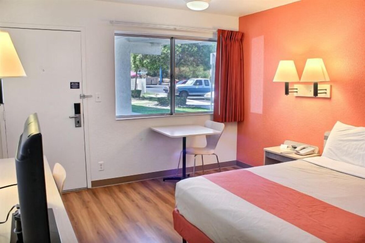 A hotel room with a bed, a desk, and a window with a view of the outside.